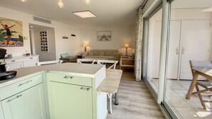 A modern kitchen with a light green color scheme, a dining area with a bench, and a large sliding glass door leading to an outdoor area. - Terrace Apartment Near the Beach (Cagnes-sur-Mer)