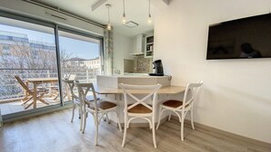 A modern kitchen with a dining area, large windows, and a flat-screen TV. - Terrace Apartment Near the Beach (Cagnes-sur-Mer)