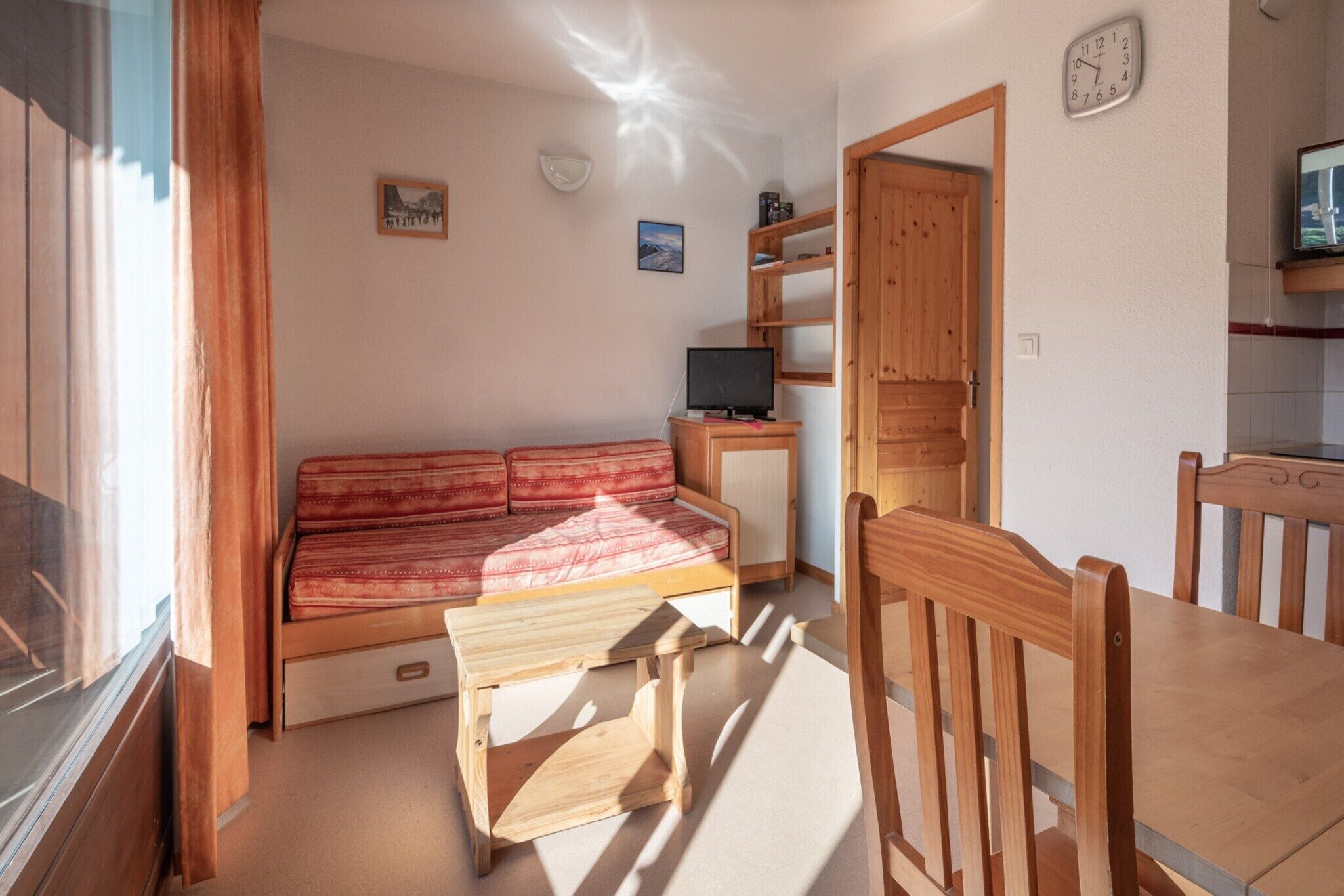 Quarto aconchegante com sofá de madeira, uma mesa pequena, televisão e mesa de jantar de madeira com cadeiras.
