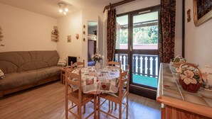 A cozy living room with a sofa, a dining table with chairs, a small kitchen area, and a balcony with patterned curtains. - Apartment in Morillon at Ski Slope (Morillon)