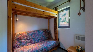 A cozy room with a bed, a small table with flowers, a window with a view, and a heater. - Apartment in Morillon at Ski Slope (Morillon)