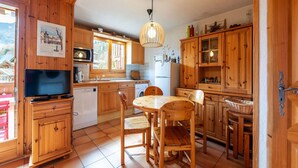 A wooden kitchen with a dining table and chairs, a television, and cabinets.