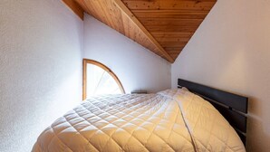 A bedroom with a wooden ceiling, a round window, and a bed with a quilted blanket.