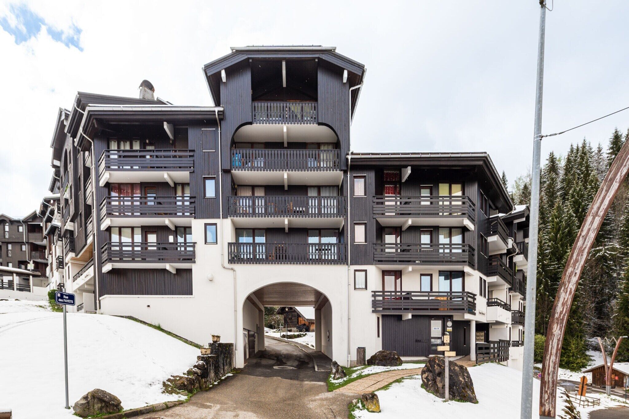 Un edificio de varios pisos con balcones, un arco de entrada y alrededores nevados.