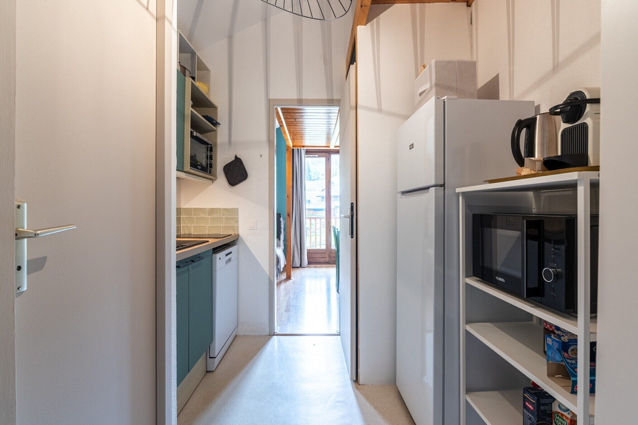 A narrow kitchen with white cabinets, a microwave, and a refrigerator.