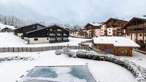 A snow-covered ski resort with multi-story buildings, including a lodge with balconies and a separate building with a wooden facade.