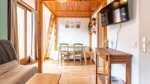 A cozy room with a wooden ceiling, a TV mounted on the wall, a wooden table, and a sofa.