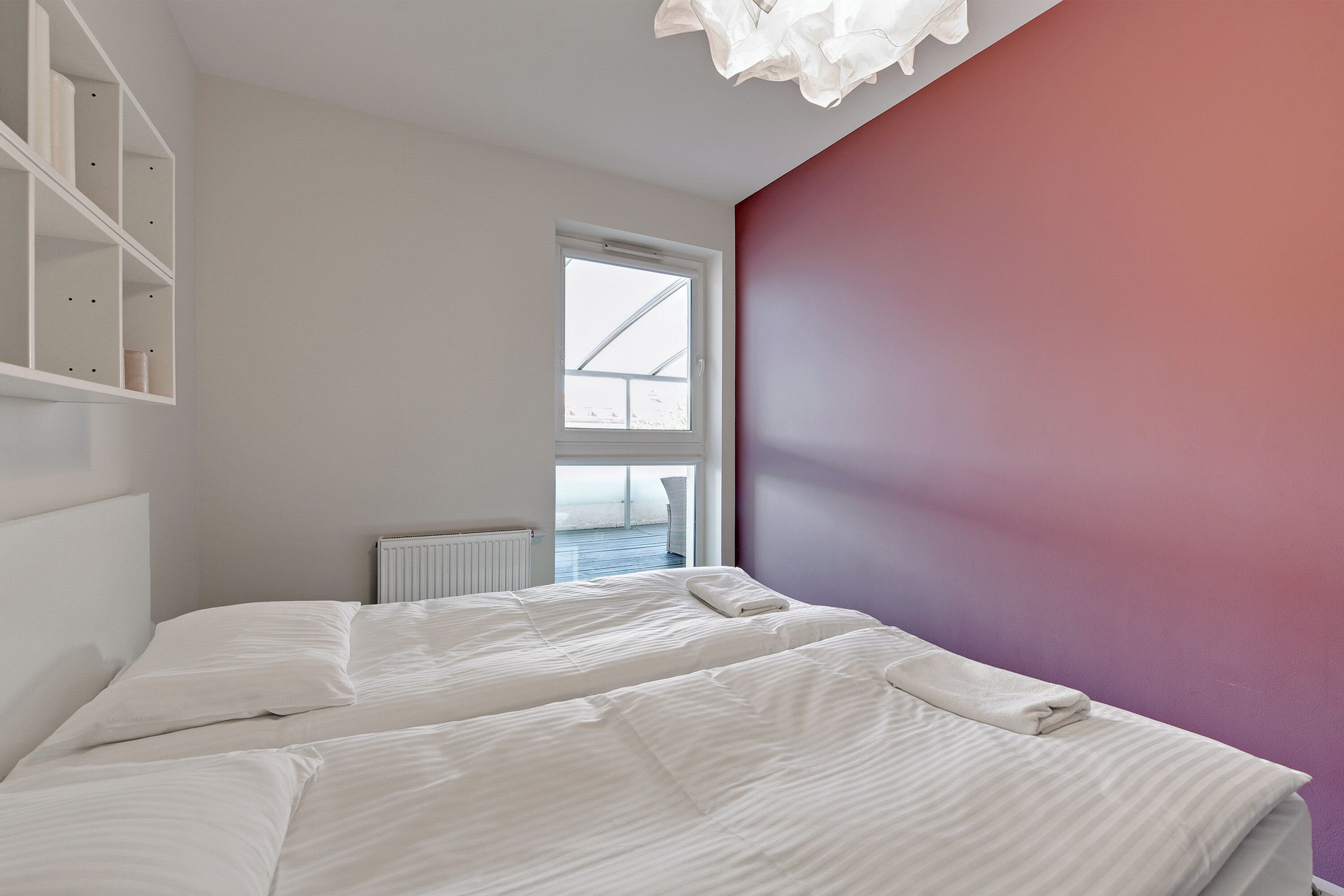 A bedroom with two beds, a window, and a white shelving unit.