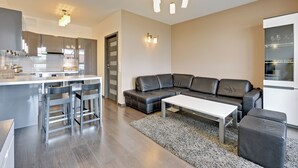 Una sala de estar moderna con un sofá gris, una mesa de centro blanca y una cocina con encimera blanca y taburetes de bar.