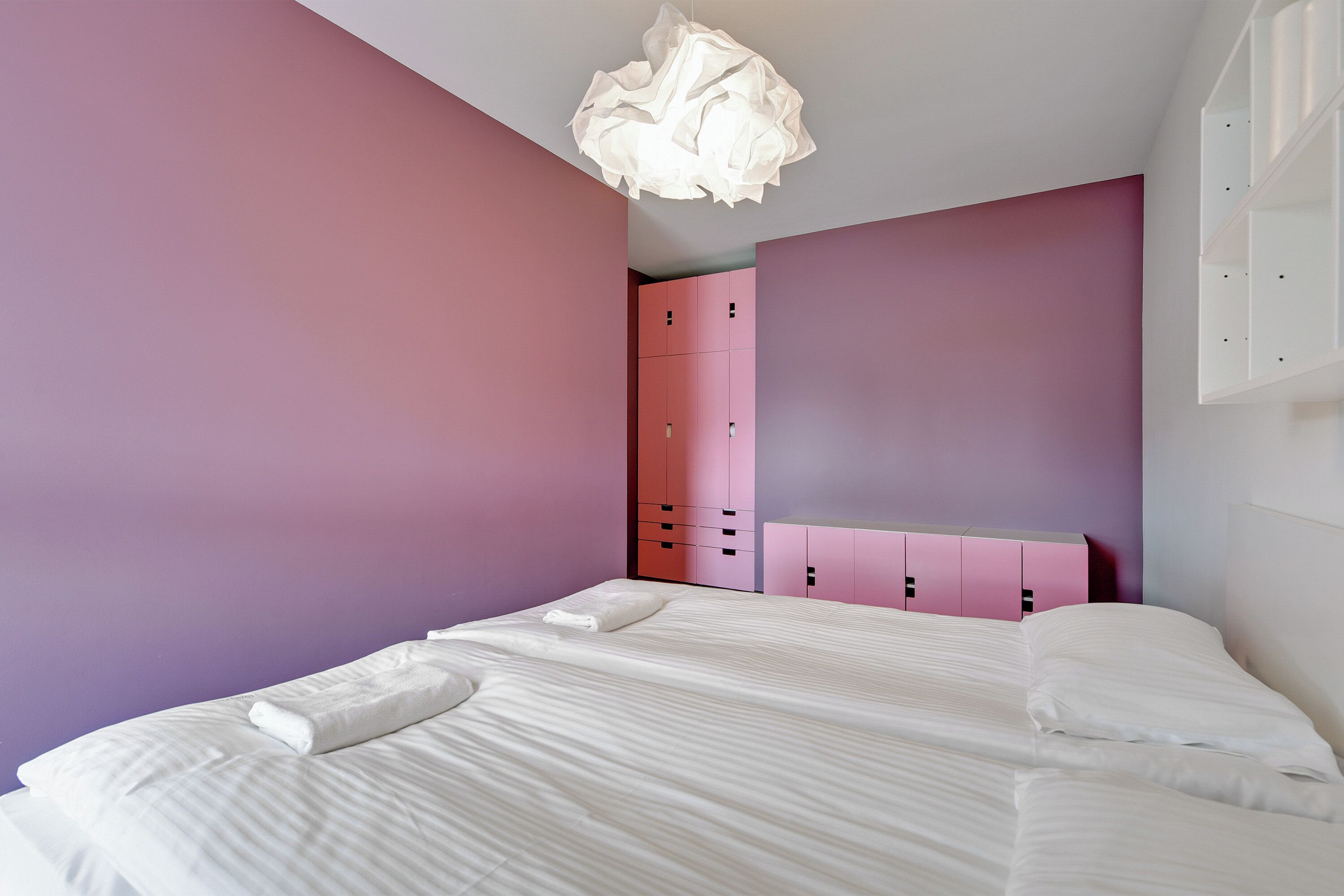 Una camera da letto con un letto, un armadio rosa e una lampada a soffitto bianca.