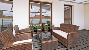 Un espacio al aire libre con techo, con mobiliario de mimbre y una mesa de vidrio, rodeado de amplias ventanas.