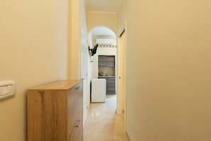 A narrow hallway with a wooden cabinet, a white refrigerator, and a kitchen area with cabinets and a sink.