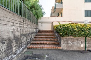 Eine Reihe aus Ziegelstufen führt zu einem Gebäude. An einer Seite eine Betonmauer, an der anderen eine mit Blumen bewachsene Mauer.