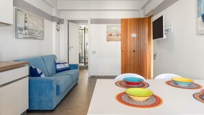 A modern living room with a blue sofa, a dining table with colorful bowls, and a TV mounted on the wall.
