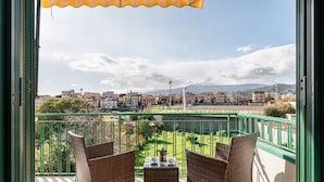 A balcony with wicker furniture, a table, and a view of a cityscape and mountains.
