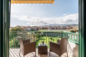 Un balcón con mobiliario de mimbre, una mesa y vistas a un paisaje urbano y montañas.