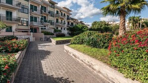 Un edificio residencial con varios balcones, un sendero pavimentado y abundante vegetación.