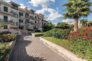 A residential building with multiple balconies, a paved pathway, and lush greenery.