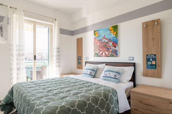 A bedroom with a bed, a painting, a window with curtains, and a wooden cabinet.