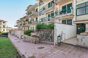 A row of multi-story residential buildings with balconies, a paved walkway, and a small grassy area.