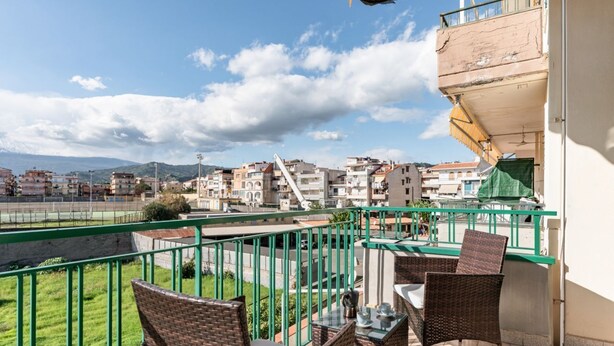 Un balcón con mobiliario de mimbre, vistas a una zona residencial y barandilla verde.
