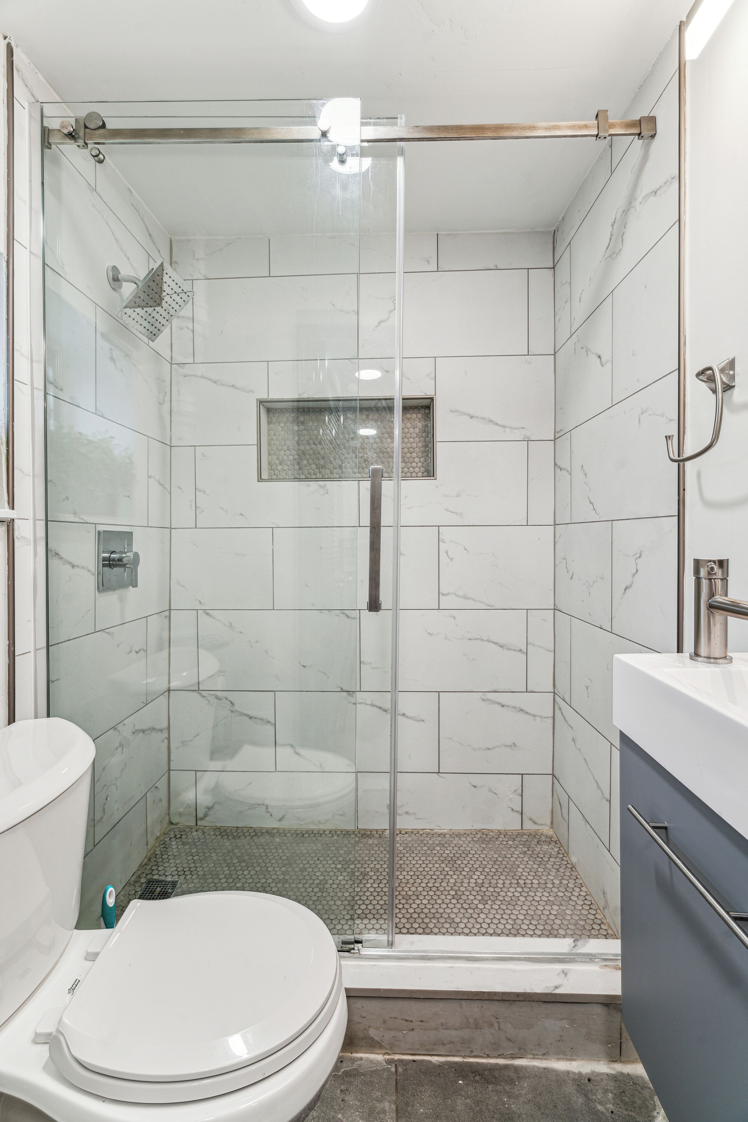 A modern bathroom with a glass-enclosed shower, a white toilet, and a marble-tiled shower area.