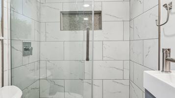 A modern bathroom with a glass-enclosed shower, a white toilet, and a marble-tiled shower area.
