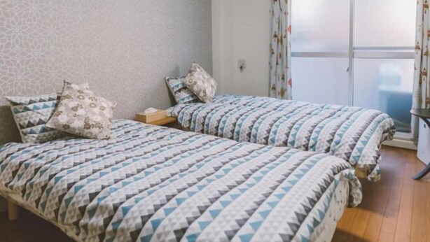 A room with two beds, each with patterned bedding, a small bedside table, and a window with curtains. - Osaka Sunshine Tower71 (Osaka)