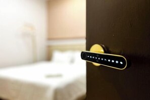 A room with a bed, a door with a numeric keypad lock, and a wall-mounted light fixture. - mana mana hotel • Melaka • (Melaka)