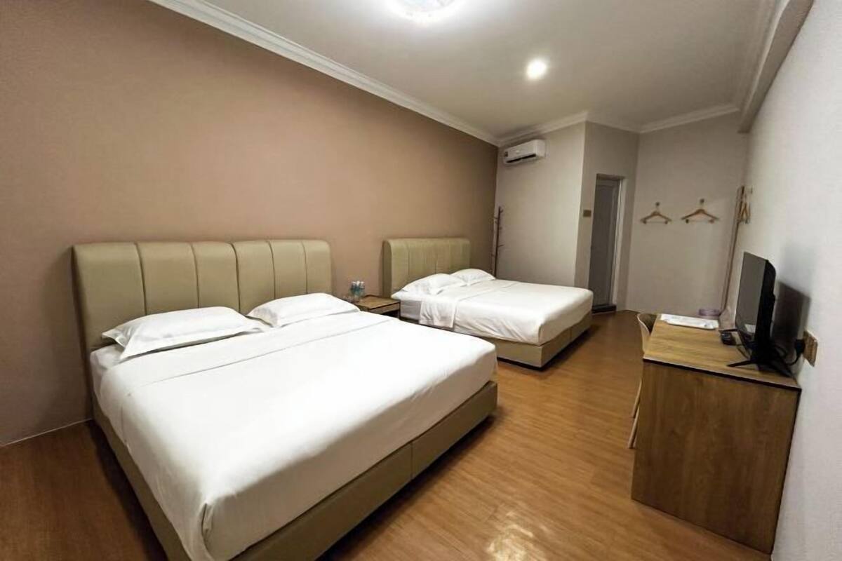 A hotel room with two beds, a wooden floor, a desk with a computer, and a TV.