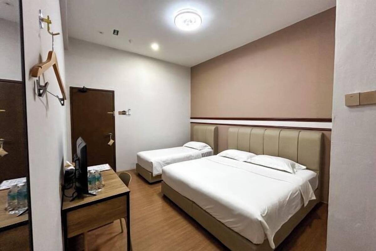 A hotel room with two beds, a desk with a chair, a mirror, and a wardrobe.