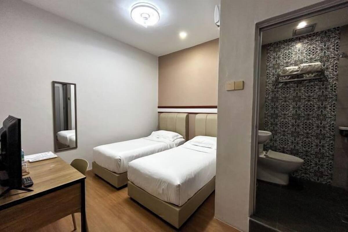 A hotel room with two beds, a desk with a computer, a mirror, and a bathroom with a patterned wall.