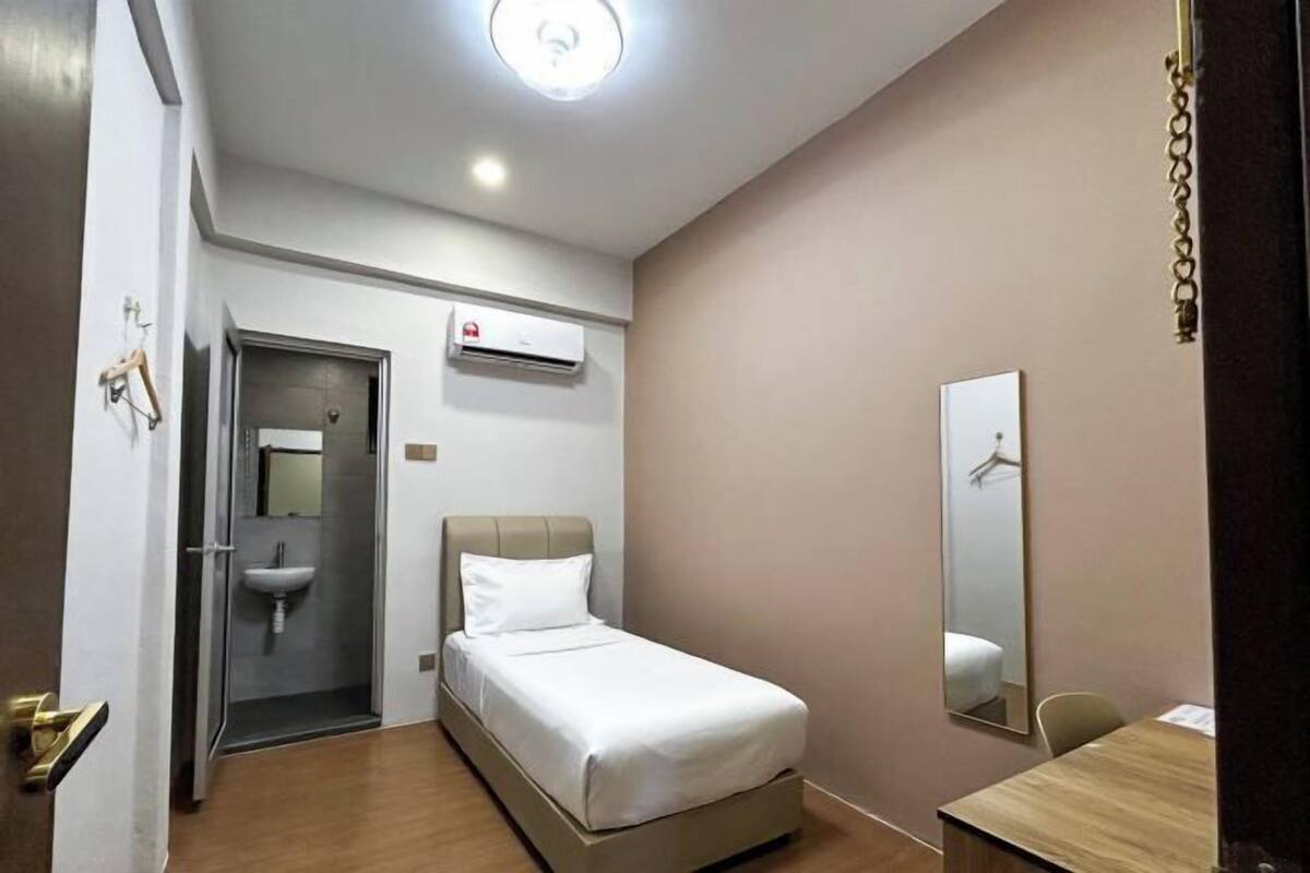 A hotel room with a bed, a desk, a mirror, a sink, and an air conditioning unit.