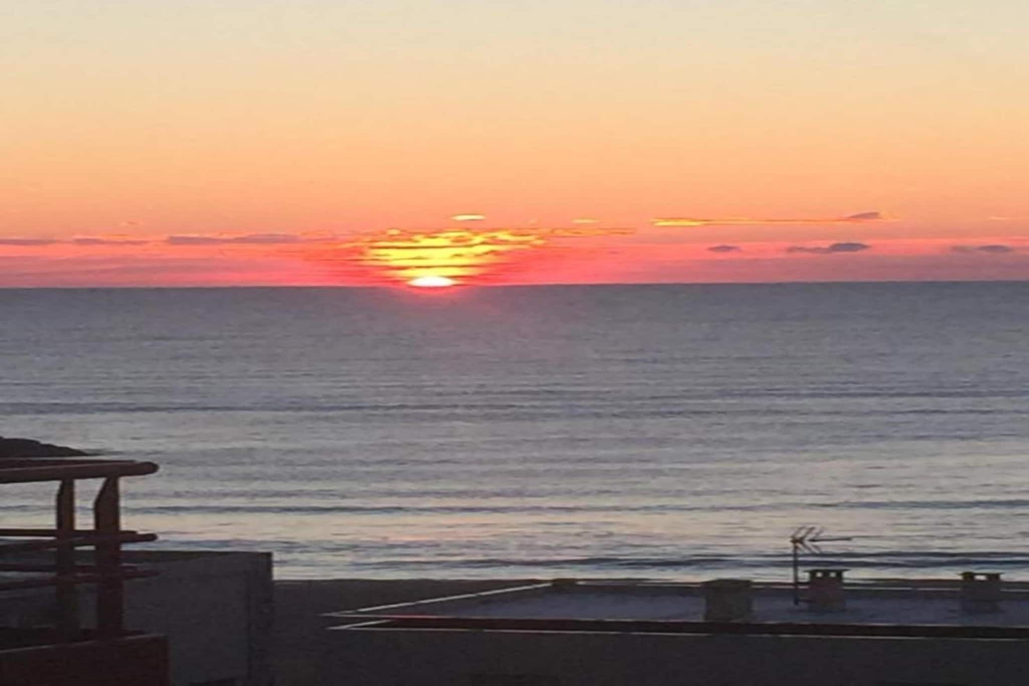 A sunset over the ocean with a view of the sea and a building with a balcony.