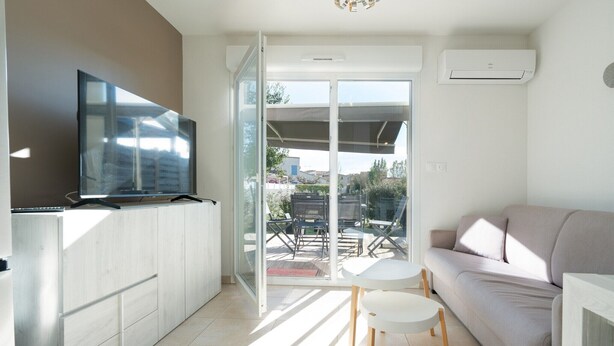 A modern living room with a sofa, a TV, a small table, and a sliding glass door leading to an outdoor patio. - Peaceful Villa in Sérignan (Sérignan)