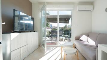 A modern living room with a sofa, a TV, a small table, and a sliding glass door leading to an outdoor patio.