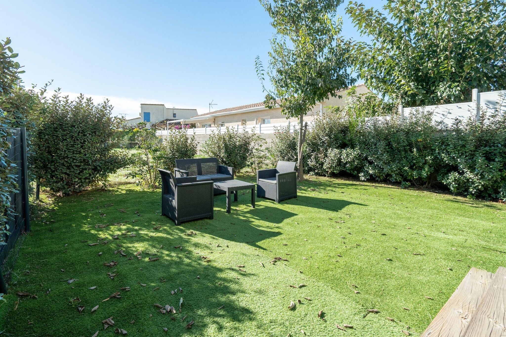Un espace extérieur aménagé avec soin, comprenant une terrasse, une pelouse verdoyante, des meubles en osier et une table en bois.
