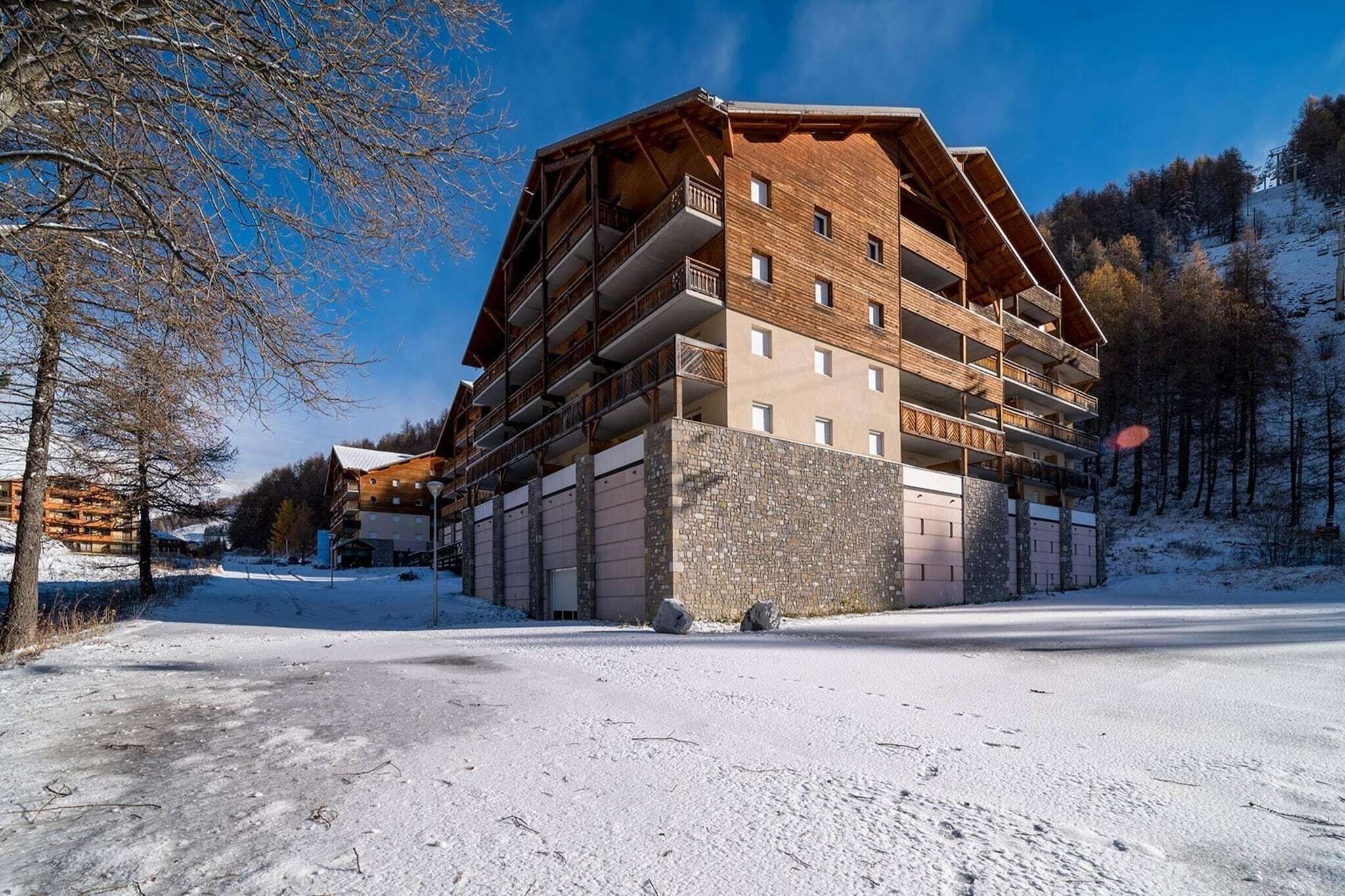 A multi-story hotel with a wooden facade and balconies, situated in a snowy landscape with trees in the background.