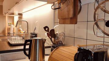 Een moderne keuken met een roestvrijstalen waterkoker, een houten snijplank en hangend keukengerei.