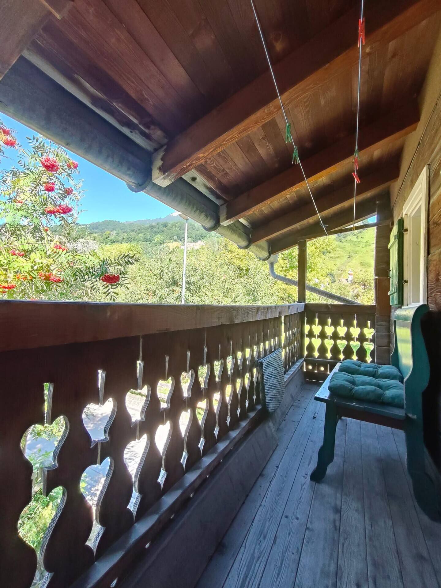 Ein Holzbalkon mit herzförmigen Ausschnitten, einer gepolsterten Bank und Blick auf Gr ünflächen und Berge.