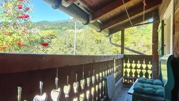 Un balcón de madera con recortados en forma de corazón, un banco acolchado y vistas a zonas verdes y montañas.