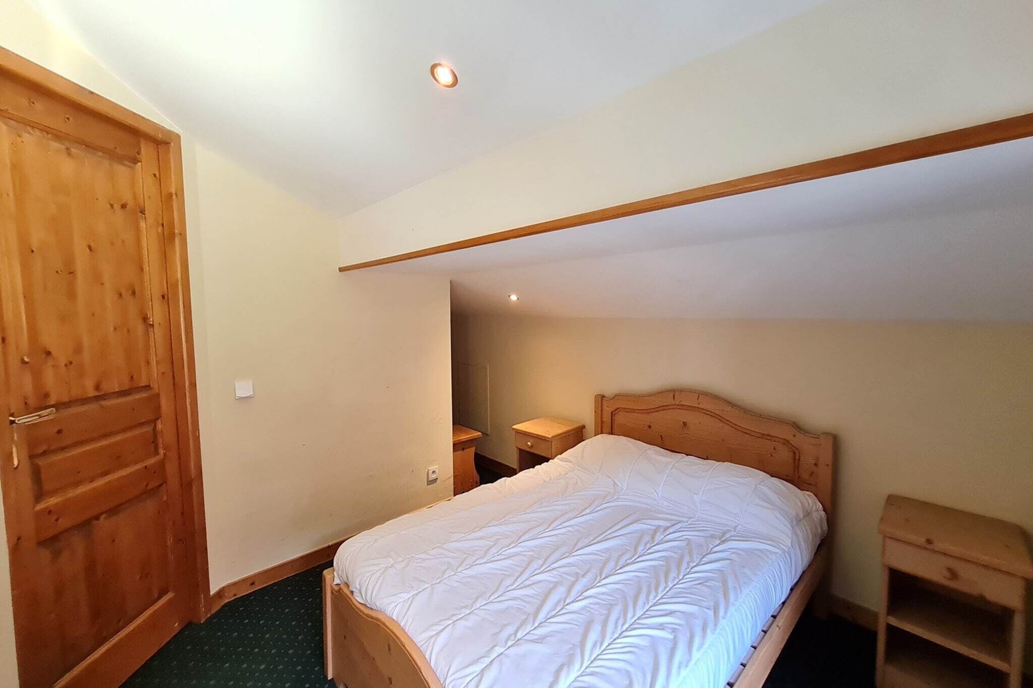 A bedroom with a wooden bed, a nightstand, a small wooden shelf, and a wooden door.