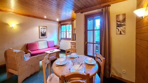 Una habitación acogedora con techo de madera, un sofá rosa, una mesa de comedor con platos y vasos, y una ventana con cortinas.