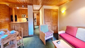 Interior acogedor de una cabaña con paredes y techos de madera, una zona de comedor con mesa y sillas, un sofá y una pequeña cocina americana.