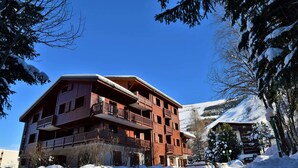 Un edificio de madera de varios pisos con balcones, rodeado de árboles cubiertos de nieve y una montaña al fondo.