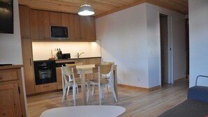 A compact kitchen with wooden cabinets, a microwave, and a dining area with a table and chairs. - Mountain Retreat for 6 Guests (Les Deux Alpes)