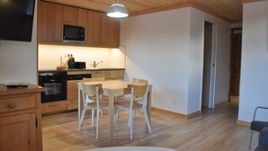 A compact kitchen with wooden cabinets, a microwave, and a dining table with chairs. - Mountain Retreat for 6 Guests (Les Deux Alpes)