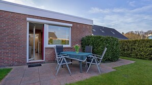 A modern house with a brick exterior, a sliding glass door, a patio with a table and chairs, and a well-maintained garden.
