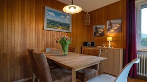 A wooden-paneled room with a dining table, chairs, a vase of flowers, a lamp, and artwork on the walls.