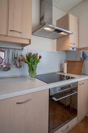 A kitchen with wooden cabinets, a stainless steel range hood, a built-in oven, and a glass vase with flowers on the countertop. - Holiday Home 'Sonneninsel' with Private Terrace, Garden and Wi-Fi (Berumbur)